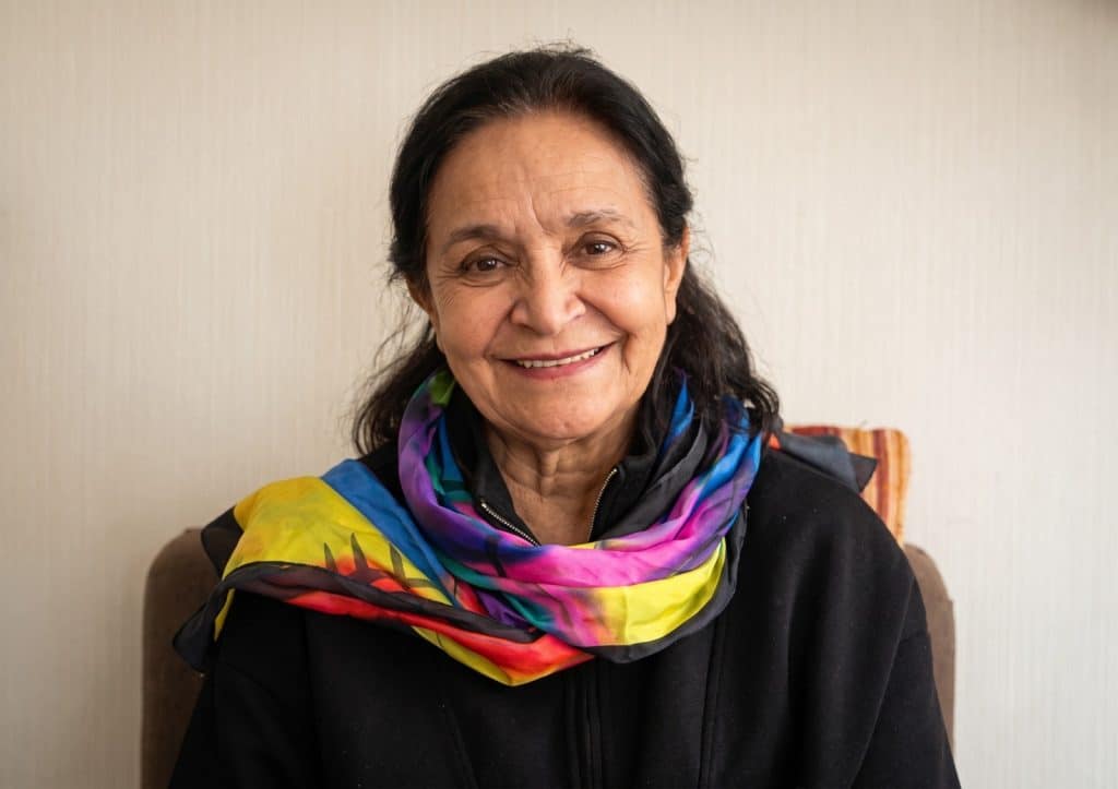 Retrato cálido y sonriente de Niniza, la autora de la columna 'La emergencia climática en los territorios que no sale en los medios', vistiendo una bufanda de seda de colores vibrantes.