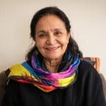 Retrato cálido y sonriente de Niniza, la autora de la columna 'La emergencia climática en los territorios que no sale en los medios', vistiendo una bufanda de seda de colores vibrantes.