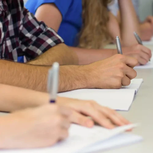 Varios estudiantes sentados en una mesa larga tomando apuntes en sus cuadernos durante las prácticas profesionales en nuestra Fundación